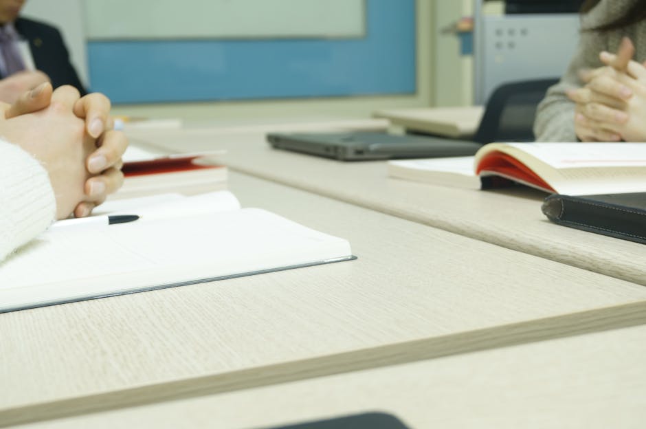 Close-up of a professional meeting setup with hands, laptops, and notebooks on a wooden desk